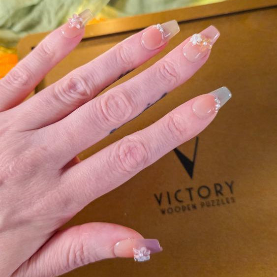 Hand with decorative nails in front of a brown box labeled 'Victory'.