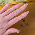Hand with decorative nails in front of a brown box labeled 'Victory'.